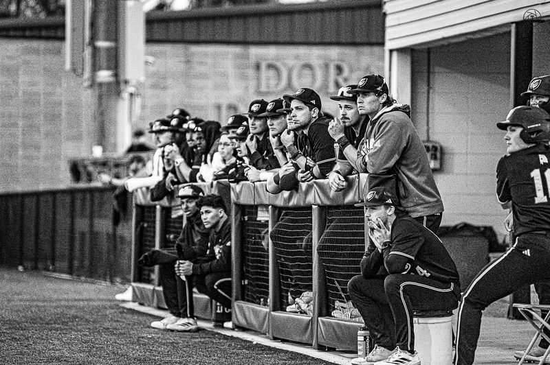 Black and white photo of a baseball dugout watching the field through the rail