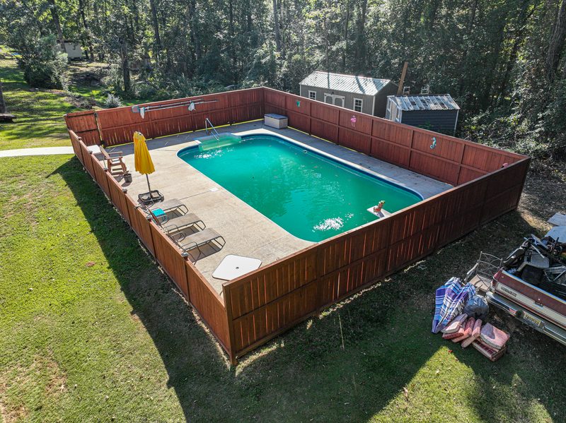 Drone photo of a fenced in ground pool with lounge chairs in a mown back yard