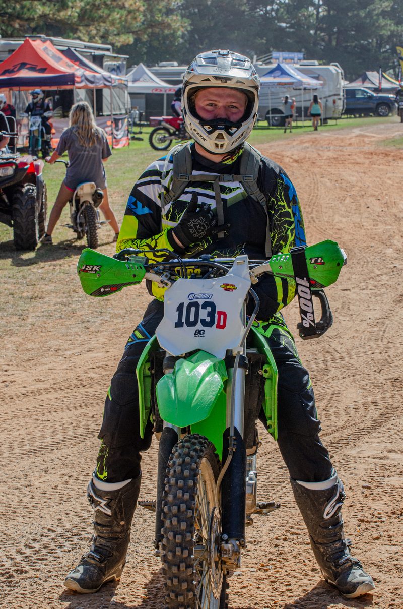 Two riders in green and black gear standing with their bikes in the paddock