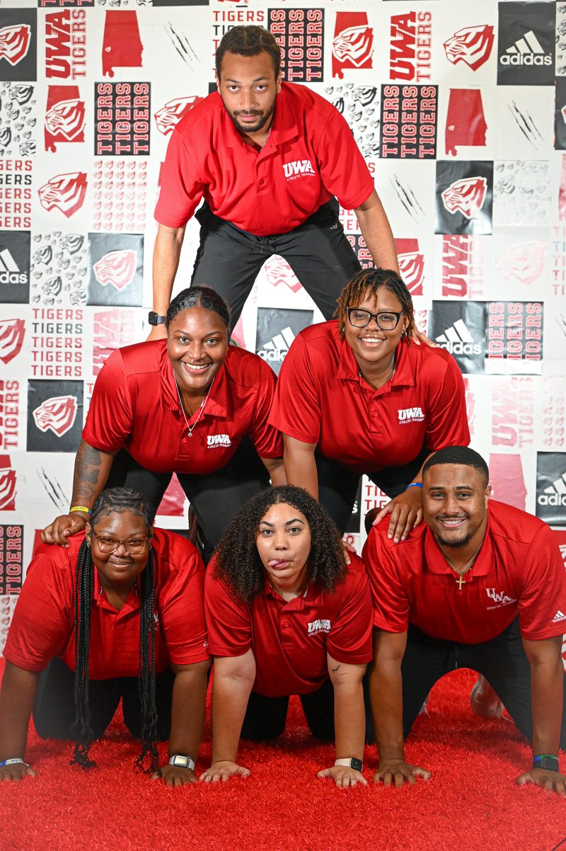 Group portrait of a West Alabama athletics staff in front of a branded backdrop